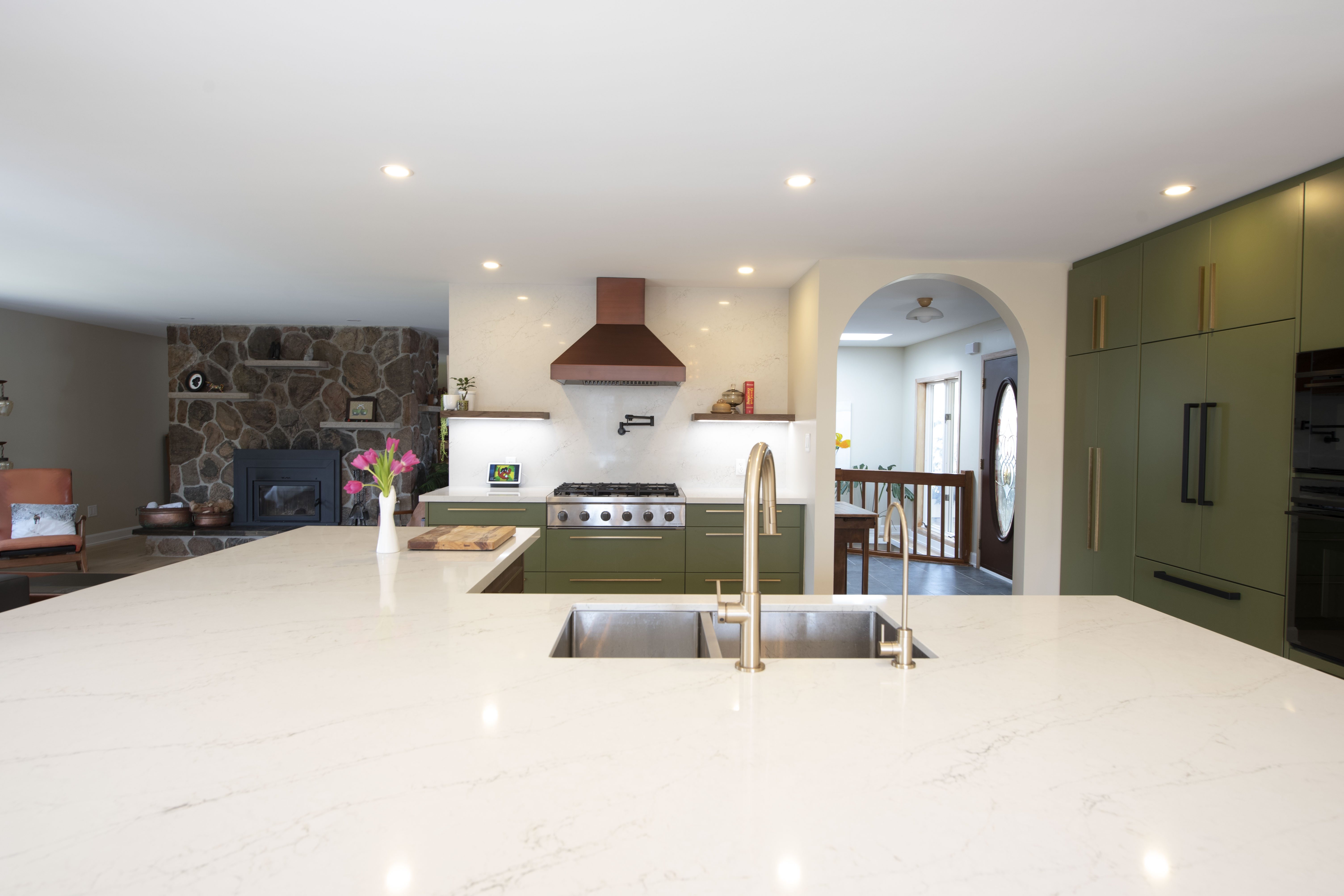 Green kitchen open to living room with stone fireplace